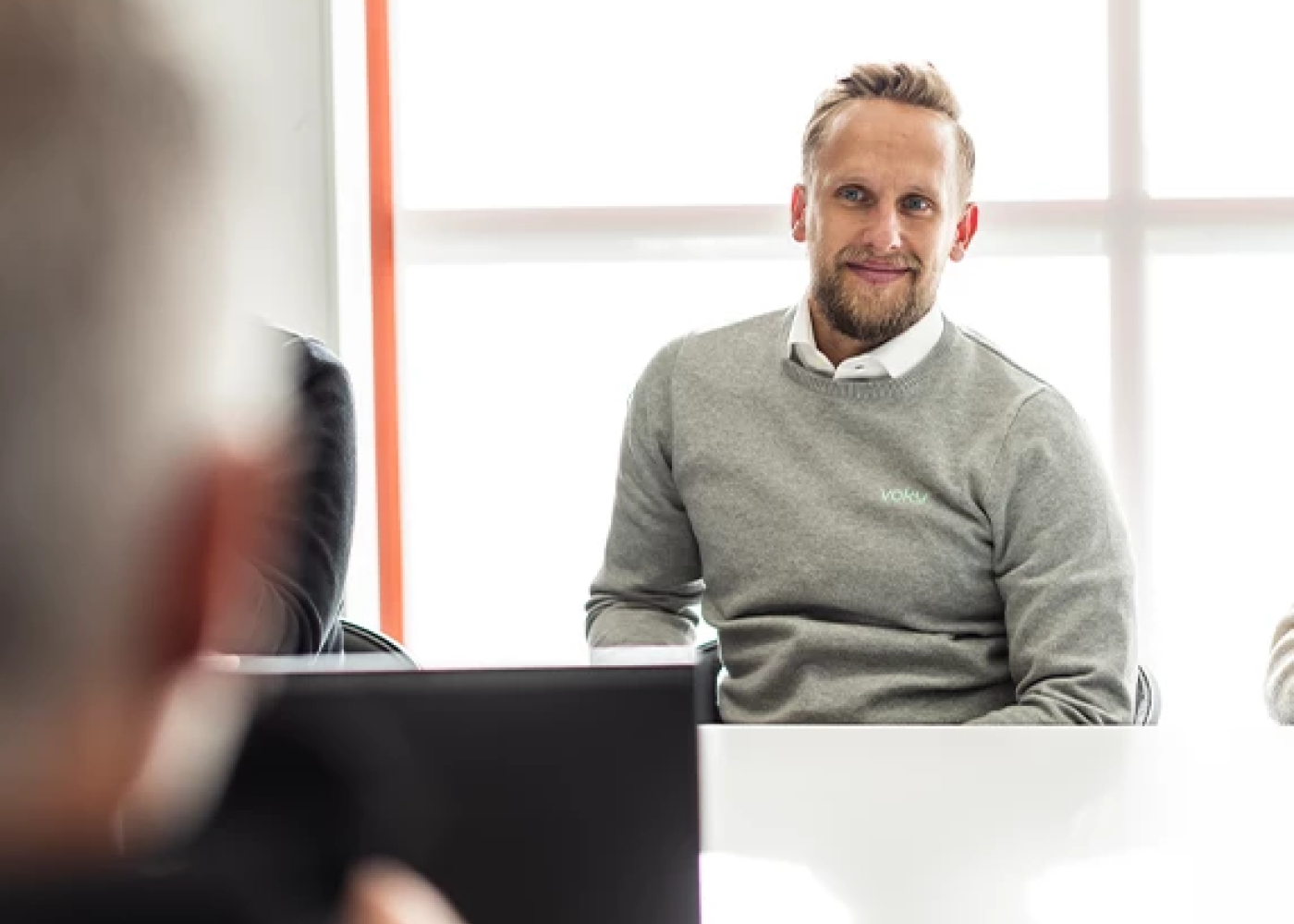 Voky-anst&auml;lld i gr&aring; sweatshirt med logotyp ler mot n&aring;gon.
