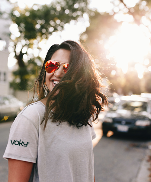 Leende kvinna i Voky-tröja och solglasögon med håret delvis över ansiktet