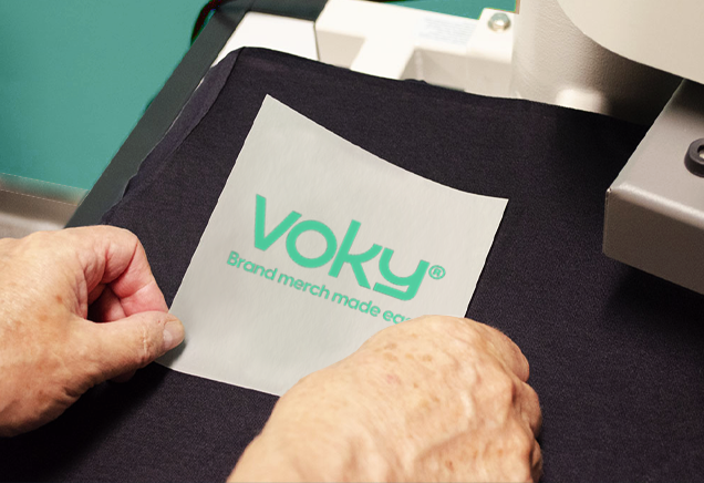Voky-logotypen tryckt på pappershållare, placerad på svart tyg för transfertryck.